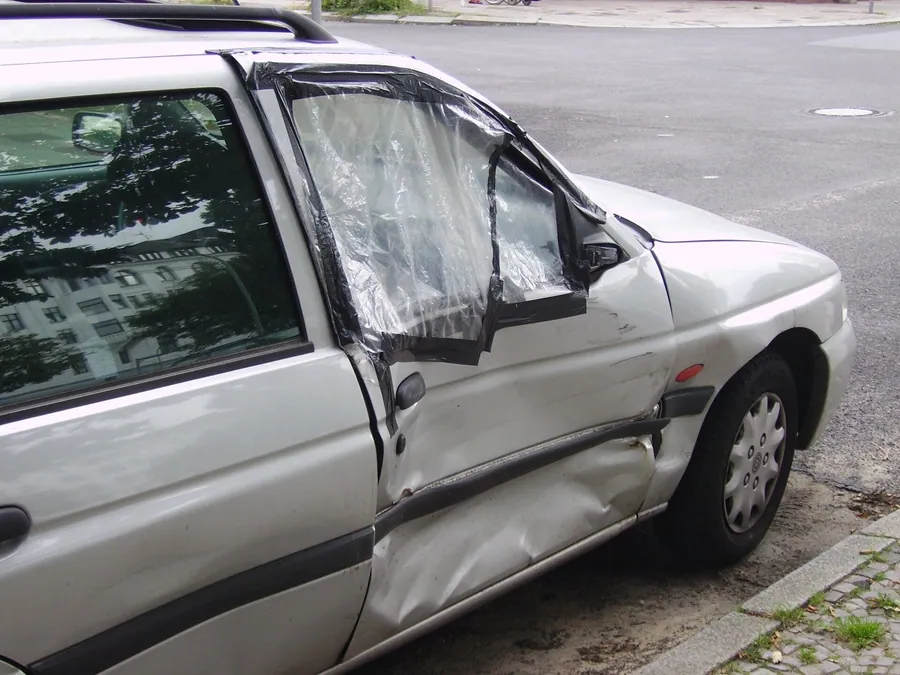 Yan kapısı çökmüş, camı kırılıp naylonla kapatılmış gümüş renkli station wagon otomobilin kaporta hasarı yakın çekimde